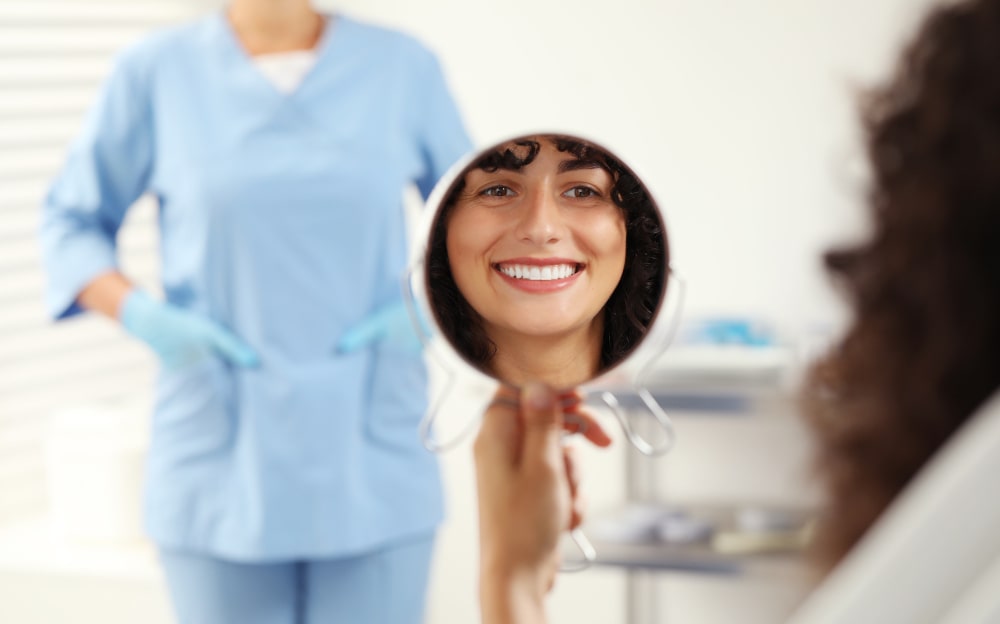 Patient looking in the mirror after cosmetic veneer placement with the dentist